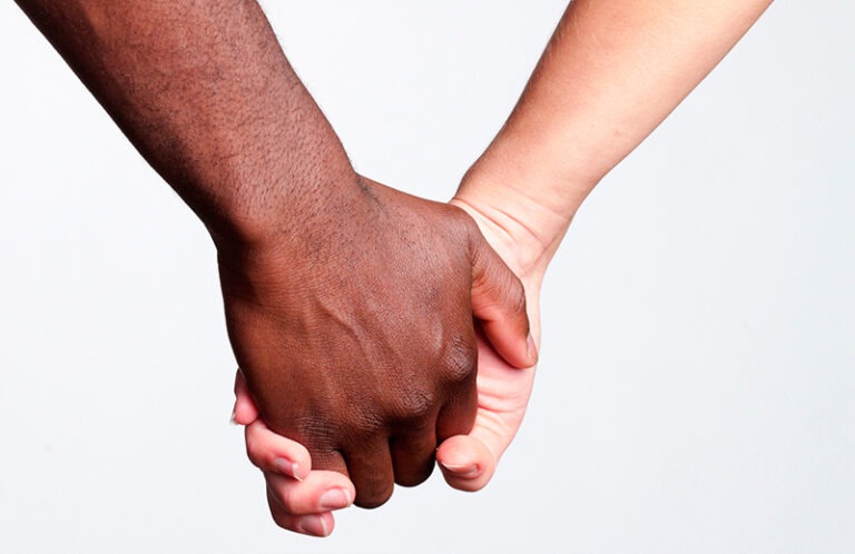 To mennesker med ulik hudfarge holder hverandre i hendene