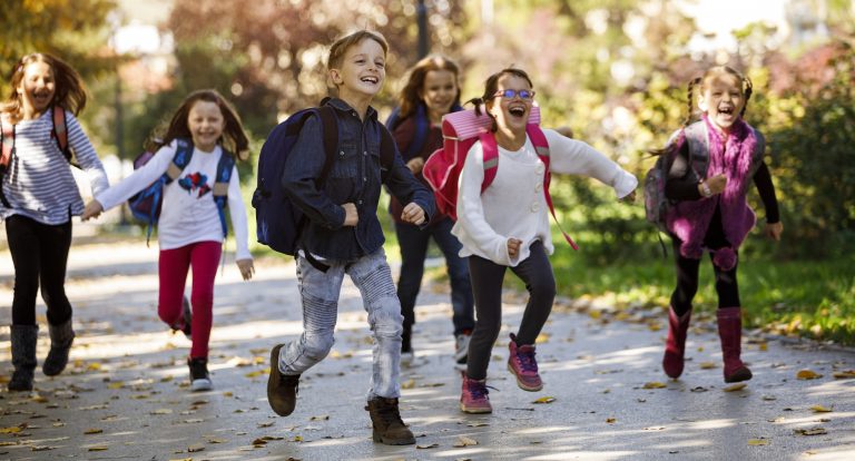 Skolestart - barn løper mot kamera og smiler med ryggsekk. Det er høst