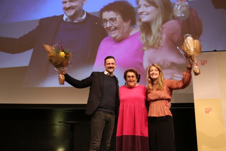 Olaug Bollestad, Dag Inge Ulstein og Ingelin Noresjø står på scenen og holder blomsterbuketter høyt opp i været. Alle smiler og er glade